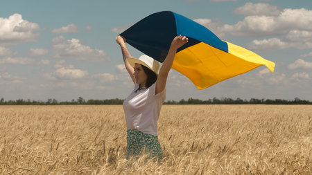 Ukrainian patriotic woman stands in wheat field and holds a blue-yellow flag of Ukraine