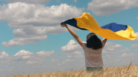 Ukrainian patriotic woman stands in wheat field and holds a blue-yellow flag of Ukraine. Back view. Copy spaceの写真素材