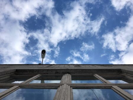 Street lamp hanging on the wall of the building against the blue sky, the sky is reflected in the windowsの写真素材