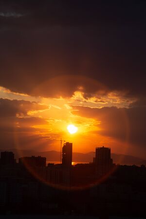 Construction crane at sunset on a background of orange sun, a city by the sea.の写真素材