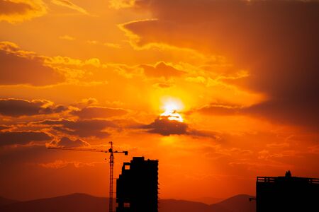 Construction crane at sunset on a background of orange sun, a city by the seaの写真素材