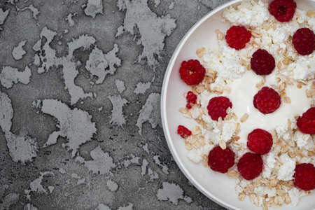 Cottage cheese is in a plate with sour cream, sprinkled with raspberries and muesli with yogurt, with a metal spoon.の写真素材