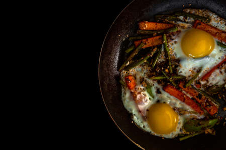 Two fried eggs in a pan with large slices of carrots, bell pepper and asparagus with spices and sauce. Close.の写真素材
