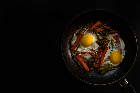 Two fried eggs in a pan with large slices of carrots, bell pepper and asparagus with spices and sauce.の写真素材