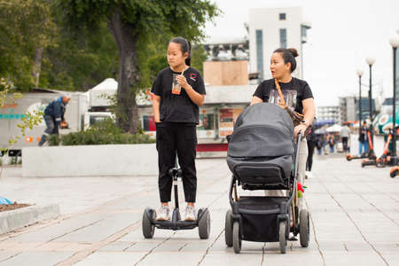 Mom and her Asian daughter driving down the street during the day. Asian girl riding a gyroscooter. Mom with a stroller.のeditorial素材