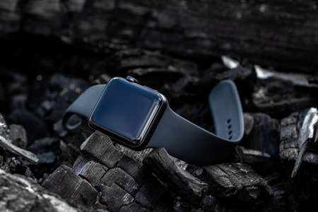 A modern electronic watch on the arm is laying on the coals. Black watch with a rubber strap.の写真素材