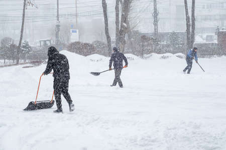 Three male workers remove snow with shovels and scrapers. It is snowing heavily outside. The snowfall.の写真素材