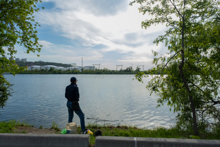 A man fishes in a lake in the city. Urban atmosphere on the shore of the lake.の写真素材