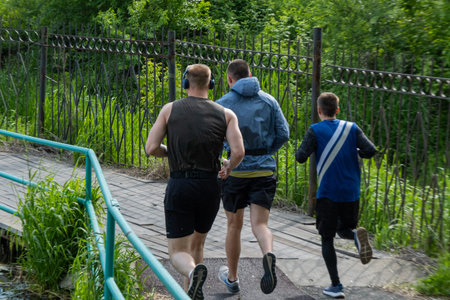 Three people running across the bridge in sportswear. An athlete wearing headphones is running.の写真素材