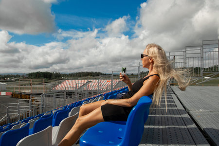 A solitary blonde woman enjoys her time watching an event or waiting for it to start in the empty...