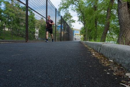 A young guy in an athletic uniform, wearing shorts runs straight down the rubber track. Sports on...
