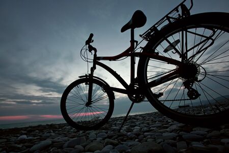 Bicycle life, The bicycle costs on stones near to sea coast against the evening skyの写真素材