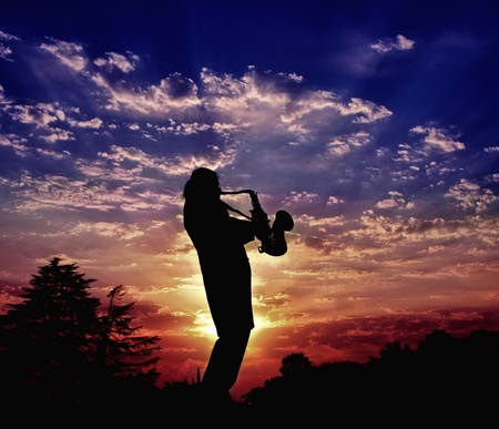 The saxophonist plays a saxophone. Harmony of sounds of a saxophone and beauty of the nature sunsetの写真素材