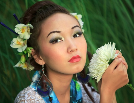 Japanese girl holds flower, against green grassの写真素材