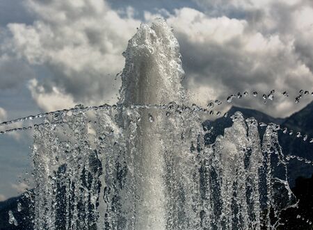 Fountain spray against the background of mountains and cloudsの写真素材
