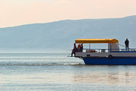 Fishing from the standing ship on island Olkhon on lake Baikal. The ship working screw creates flow on which the fish approachesのeditorial素材