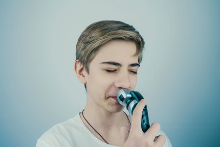Teenage boy is shaving at first time his mustaches with an electric razor. Young man shaves his face with a electric razor.の写真素材