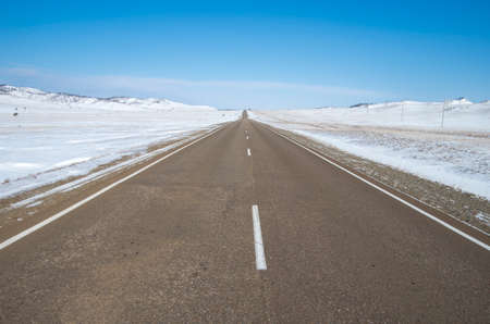 Winter road to the mountains. Asphalt road and mountains with winter landscape snow lies on the roadside.の写真素材