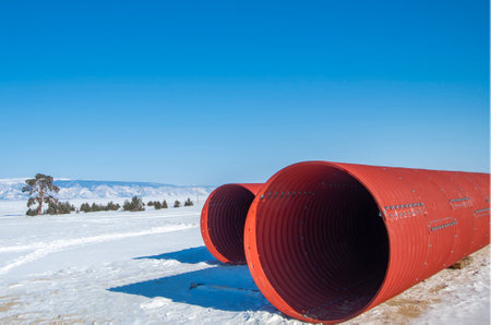 Pipeline, red metal pipes in winter lie on the snow against the background of a cloudless blue sky.の写真素材