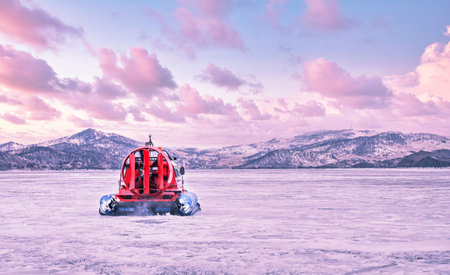 Hovercraft quickly glides over the surface of the transparent frozen Lake Baikal at sunset, winter...