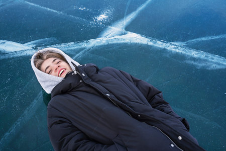 Teenager lies on his back on the frozen ice of Lake Baikal.