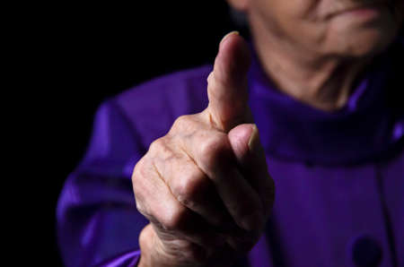 Elderly lady is shaking her fingera black background.の写真素材