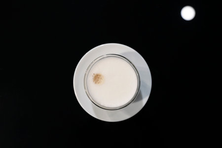Cup of coffee cappuccino with frothy foam on a black glass table. View from above.