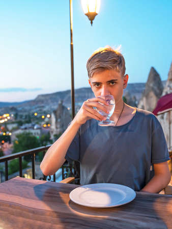 Teenager with a glass of water on a view of Goreme at night in Cappadocia. Vertical.の写真素材