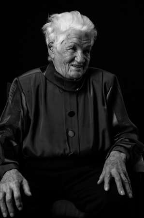 Portrait of an aged woman looking away on a black background. Black and white photo, vertical.の写真素材