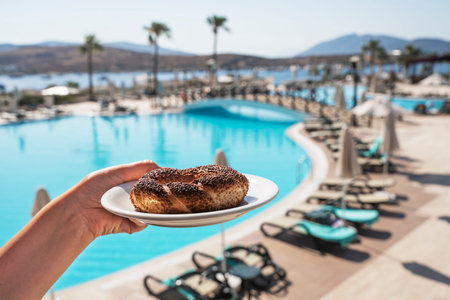 Turkish bagel on a saucer in hand against the backdrop of the blue sea and palm trees. National...
