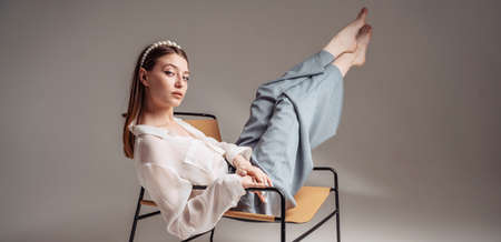Casual young woman sits barefoot on a comfortable armchair, relaxes, raises her legs. Feet up.の写真素材