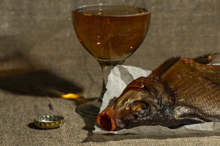 Glass of beer with cork and dried fish on paper for cutting fishの写真素材