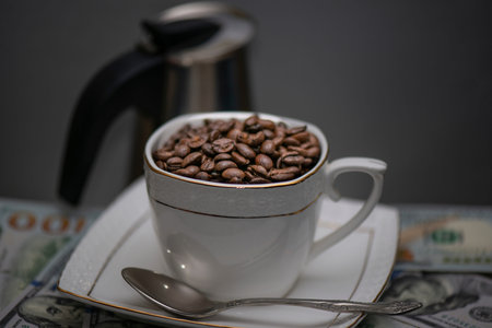 White Cup on saucer with coffee beans on grey background with coffee pot