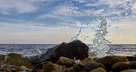 waves run onto shore and crash against the rocks, creating many splashes and splashes near shore. river surf in stormy weather near stone pebble coast with foamy splashing waves.の写真素材