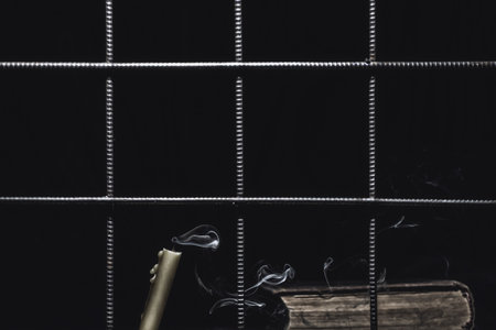 a candle and a book behind bars on a black background, an extinguished candle, smoke from a candle,...