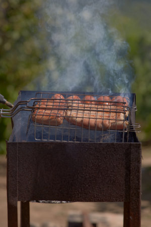 Cooking delicious and juicy sausages on the grill close-up. Roasted sausages on fire with smoke. Cooking hot food in nature on the weekendの写真素材