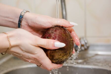 To wash beet. The woman washes beet with water. To wash dirty beet waterの写真素材