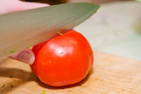 To cut a tomato. To cut tomatoes on a wooden board. Tamata for salad. Healthy food.の写真素材