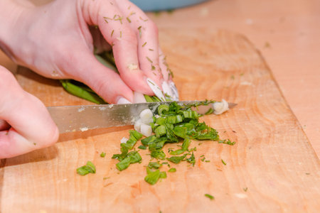 To cut green onions. The girl cuts onions on a wooden board. To cook healthy food.