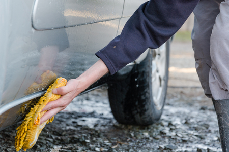 The man washes with a sponge with foam the car. To wash the car on the street in the spring. To rinse with soap water the car and wheelsの写真素材