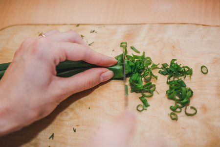 To cut green onions. The girl cuts green onions on a wooden board. Healthy foodの写真素材