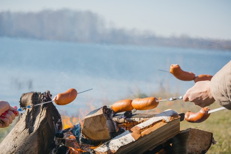 People fry sausages and bread at the stake by the lake in the eveningの写真素材