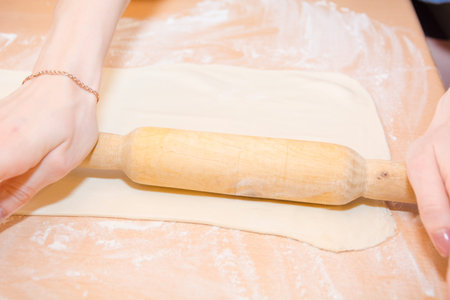 Girl tool rolls dough on a wooden table