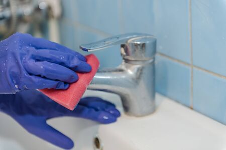 The girl is cleaning the bathroom, wash the tap in the bathroom, wash with rubber gloves, clean up the house, clean the shiny metal tapの写真素材