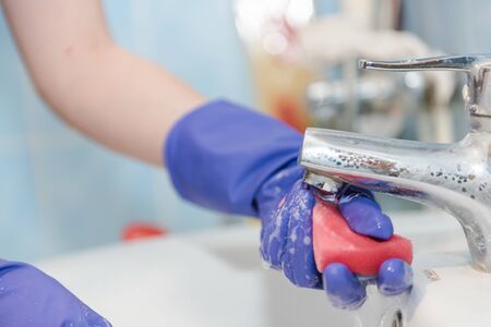 The girl cleans the bathroom, clean the ceramic sink in the bathroom, wash with rubber gloves, clean up the house, wash with a sponge and foamの写真素材