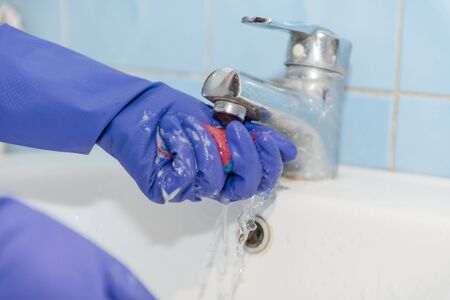 The girl cleans the bathroom, clean the ceramic sink in the bathroom, wash with rubber gloves, clean up the house, wash with a sponge and foamの写真素材