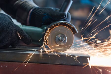 Cut metal with a Angular grinding machine. Sparks are flying. Construction tool grinder. A man is cutting metal. Wear gloves for safety. Use a dangerous tool in workの写真素材