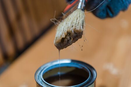 Girl with a brush paints a bench. Garden furniture. Paint with a wide brush. Varnish in a can for painting. To paint boards.の写真素材