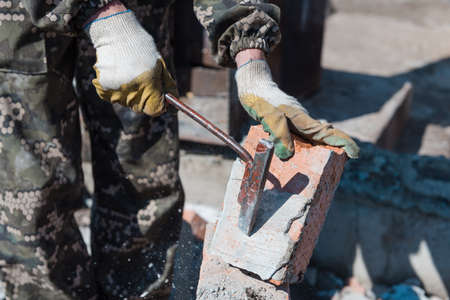 Brick in cement. Remove cement. Breaking down a brick wall. Knocking on bricks. Remove brick fragments. Cleaning the area from debris. Construction of a brick fence. Hard workの写真素材