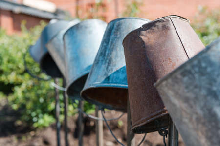Metal buckets in the garden. Water from a bucket. The bucket weighs on the fence. Tools in the garden. Agriculture. Old buckets. Village lifeの写真素材